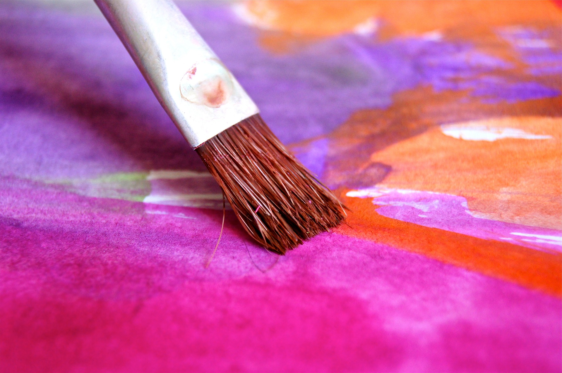 A thin paintbrush runs on top of bright pink and orange pastel colors