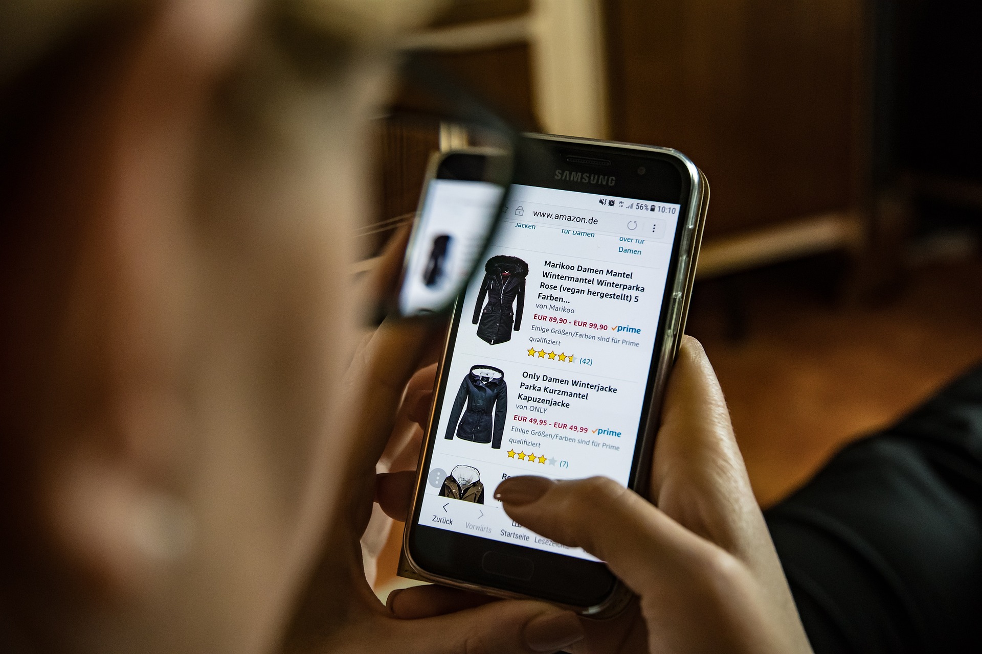 Someone holding a cellphone with jacket options on a shopping site.